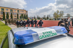 Uczniowie maszerują na miejsce zbiórki. Na pierwszym planie kogut Straż Graniczna na samochodzie. Uczniowie maszerują na miejsce zbiórki. Na pierwszym planie kogut Straż Graniczna na samochodzie.