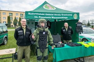 Jeden z uczniów stoi ubrany w kombinezon pirotechnika. Obok niego stoją funkcjonariusze SG. W tle namiot NwOSG. Jeden z uczniów stoi ubrany w kombinezon pirotechnika. Obok niego stoją funkcjonariusze SG. W tle namiot NwOSG.