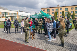 Uczniowie stoją przed namiotem NwOSG. Słuchają przewodnika psa służbowego. Uczniowie stoją przed namiotem NwOSG. Słuchają przewodnika psa służbowego.