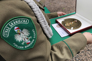 Funkcjonariuszka trzyma medal Pamiątkowy „Za Zasługi dla Nadwiślańskiego Oddziału Straży Granicznej”. Funkcjonariuszka trzyma medal Pamiątkowy „Za Zasługi dla Nadwiślańskiego Oddziału Straży Granicznej”.