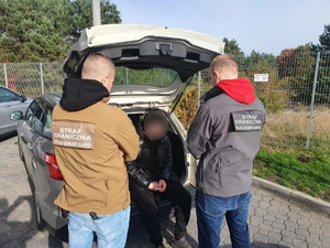 Cudzoziemiec siedzi w pojeździe. Przed nim stoją funkcjonariusze SG. Cudzoziemiec siedzi w pojeździe. Przed nim stoją funkcjonariusze SG.