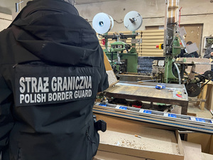 Funkcjonariusz SG stoi tyłem na tle maszyny. Funkcjonariusz SG stoi tyłem na tle maszyny.