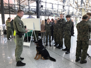 Przewodnik i pies służbowy stoją przed uczniami klasy mundurowej. Przewodnik i pies służbowy stoją przed uczniami klasy mundurowej.