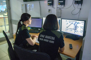 Funkcjonariuszki siedzą przed monitorami. Prowadzą nadzór nad kontrolą bezpieczeństwa. Funkcjonariuszki siedzą przed monitorami. Prowadzą nadzór nad kontrolą bezpieczeństwa.