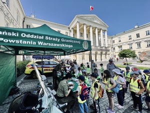 Na pierwszym planie namiot Nadwiślańskiego Oddziału straży Granicznej. Przed nim stoją dzieci. Na drugim planie ambulans. w tle budynek Urzędu. Na pierwszym planie namiot Nadwiślańskiego Oddziału straży Granicznej. Przed nim stoją dzieci. Na drugim planie ambulans. w tle budynek Urzędu.