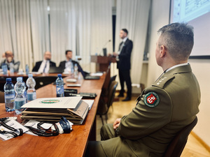 Kpt. SG Mariusz Urban siedzi przy stole w tle uczestnicy konferencji. Kpt. SG Mariusz Urban siedzi przy stole w tle uczestnicy konferencji.