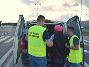 Funkcjonariusze wprowadzają cudzoziemca do samochodu służbowego. Funkcjonariusze wprowadzają cudzoziemca do samochodu służbowego.