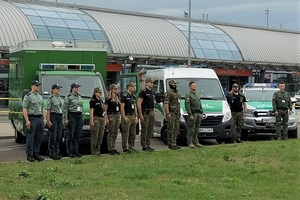 Funkcjonariusze służb stoją na tle pojazdów służbowych i terminala lotniska. Zdjęcie: FB Lotnisko Warszawa/Modlin Funkcjonariusze służb stoją na tle pojazdów służbowych i terminala lotniska. Zdjęcie: FB Lotnisko Warszawa/Modlin