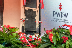 Na pierwszym planie u dołu wieńce, w tle tablica pamiątkowa. Na pierwszym planie u dołu wieńce, w tle tablica pamiątkowa.