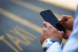 Telefon trzymany w dłoniach. W tle napis TAXI namalowany na ulicy. Zdjęcie poglądowe. Telefon trzymany w dłoniach. W tle napis TAXI namalowany na ulicy. Zdjęcie poglądowe.