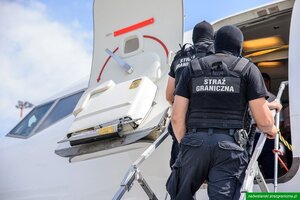Funkcjonariusze Straży Granicznej stoją na schodach przed wejściem do samolotu. Funkcjonariusze Straży Granicznej stoją na schodach przed wejściem do samolotu.