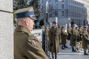 Żołnierz prezentuje broń w tle stoi orkiestra. Żołnierz prezentuje broń w tle stoi orkiestra.
