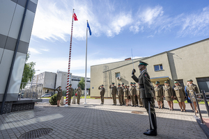 Na masztach Flaga Polski i Unii Europejskiej. Funkcjonariusze stoją w szyku oddając honory. Na masztach Flaga Polski i Unii Europejskiej. Funkcjonariusze stoją w szyku oddając honory.
