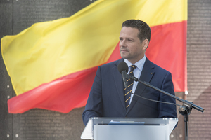 Na tle żółto-czerwonej flagi stoi Pan Rafał Trzaskowski. Na tle żółto-czerwonej flagi stoi Pan Rafał Trzaskowski.