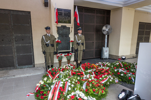Przy tablicy pamiątkowej stoją żołnierze. Przed nimi leżą wieńce i wiązanki kwiatów. Przy tablicy pamiątkowej stoją żołnierze. Przed nimi leżą wieńce i wiązanki kwiatów.
