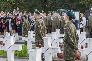 Na pierwszym planie białe krzyże między którymi stoją uczniowie szkoły, w oddali delegacja NwOSG. Na pierwszym planie białe krzyże między którymi stoją uczniowie szkoły, w oddali delegacja NwOSG.