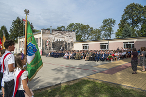 Uczestnicy uroczystości siedzą na krzesłach, na drugim planie widać mural na ścianie. Uczestnicy uroczystości siedzą na krzesłach, na drugim planie widać mural na ścianie.