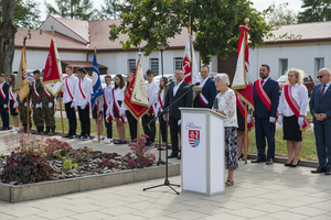 Na tle pocztów sztandarowych przy mównicy przemawia pani Maria Rrubas. Na tle pocztów sztandarowych przy mównicy przemawia pani Maria Rrubas.
