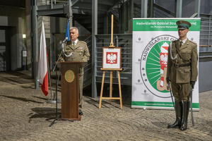Przy mównicy przemawia płk SG Dariusz Lutyński, obok stoi dowódca uroczystości. Przy mównicy przemawia płk SG Dariusz Lutyński, obok stoi dowódca uroczystości.