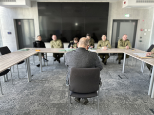 Mężczyzna siedzi na krześle. W tle siedzą funkcjonariusze z komisji. Mężczyzna siedzi na krześle. W tle siedzą funkcjonariusze z komisji.