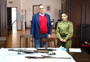 Pracownik muzeum i funkcjonariuszka Straży Granicznej stoją przed stołem, na którym leży przekazana broń. Pracownik muzeum i funkcjonariuszka Straży Granicznej stoją przed stołem, na którym leży przekazana broń.
