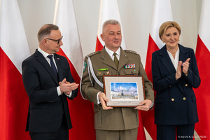 Płk SG Dariusz Lutyński prezentuje podziękowania. Po bokach stoi Para Prezydencka. Płk SG Dariusz Lutyński prezentuje podziękowania. Po bokach stoi Para Prezydencka.