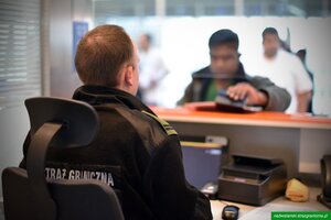 Podróżny podaje dokument funkcjonariuszowi, który siedzi w kabinie kontrolerskiej. Podróżny podaje dokument funkcjonariuszowi, który siedzi w kabinie kontrolerskiej.
