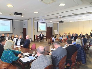 Uczestnicy spotkania siedzą przy stołach. Na ekranie wyświetlana jest prezentacja. Uczestnicy spotkania siedzą przy stołach. Na ekranie wyświetlana jest prezentacja.