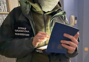 Funkcjonariusz trzyma w ręku paszport, sprawdza dane w urządzeniu mobilnym. Funkcjonariusz trzyma w ręku paszport, sprawdza dane w urządzeniu mobilnym.