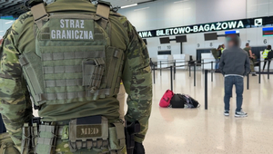 Po lewej stronie stoi funkcjonariusz. W tle cudzoziemiec oczekuje na odprawę check in. Po lewej stronie stoi funkcjonariusz. W tle cudzoziemiec oczekuje na odprawę check in.