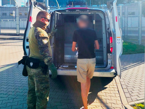 Funkcjonariusz wprowadza cudzoziemca do pojazdu służbowego. Funkcjonariusz wprowadza cudzoziemca do pojazdu służbowego.